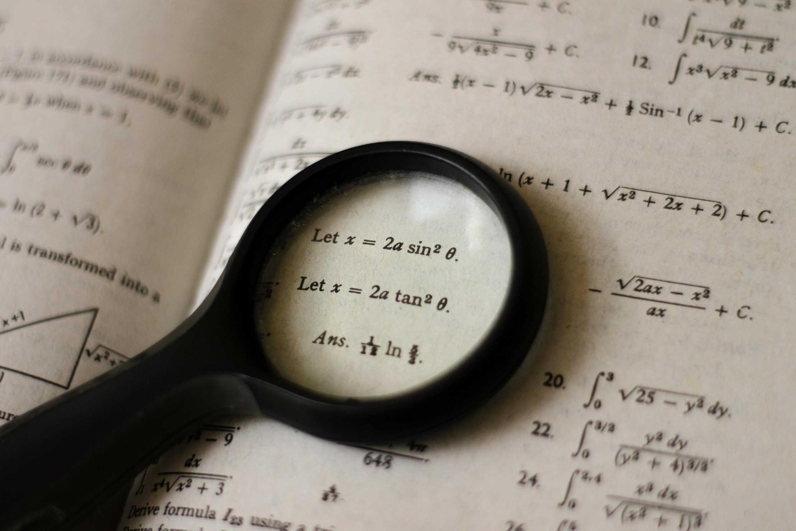 A magnifying glass focusing on mathematical equations in a textbook, symbolizing detailed study.
